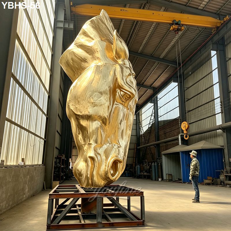 A massive, unpainted sculpture of a horse's head is on display inside an industrial facility, mounted on a metal base.