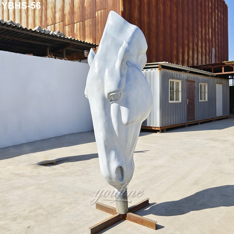 A large white horse head sculpture mounted on a metal base in an outdoor setting with industrial buildings in the background.