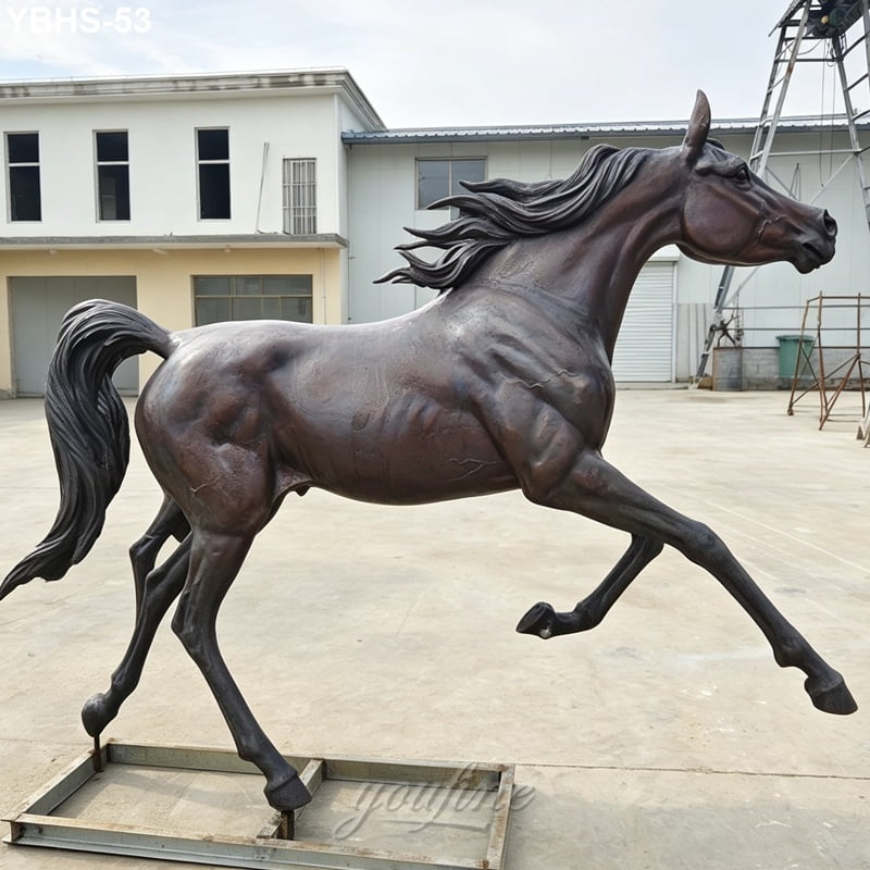 Bronze Arabian horse sculpture depicting a running horse with flowing mane, displayed outdoors near industrial buildings.