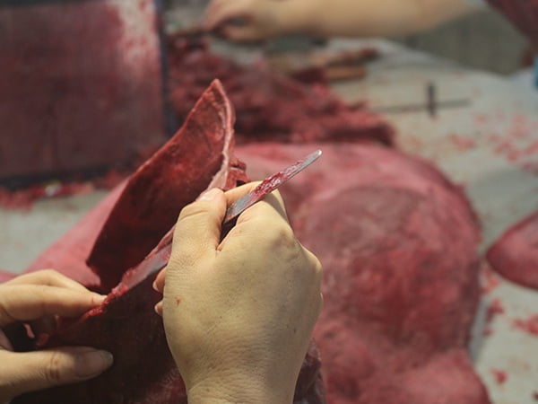 Chasing artist refining a wax horse section under directional lighting