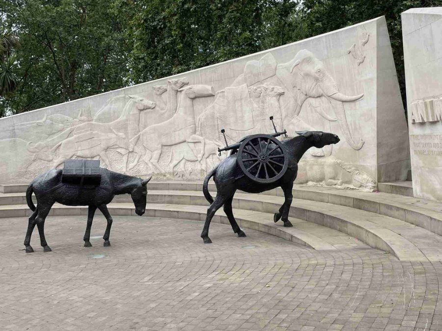 Two bronze horse in War Memorial , one with a wheel and the other with a pack, in front of carved memorial walls.