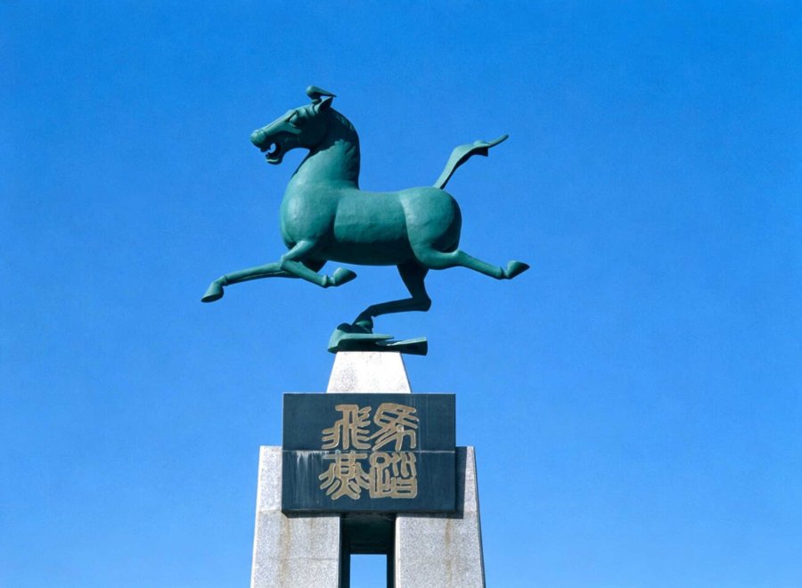 A dynamic bronze Flying Horse of Gansu mounted atop a pedestal, set against a bright blue sky with engraved text visible.