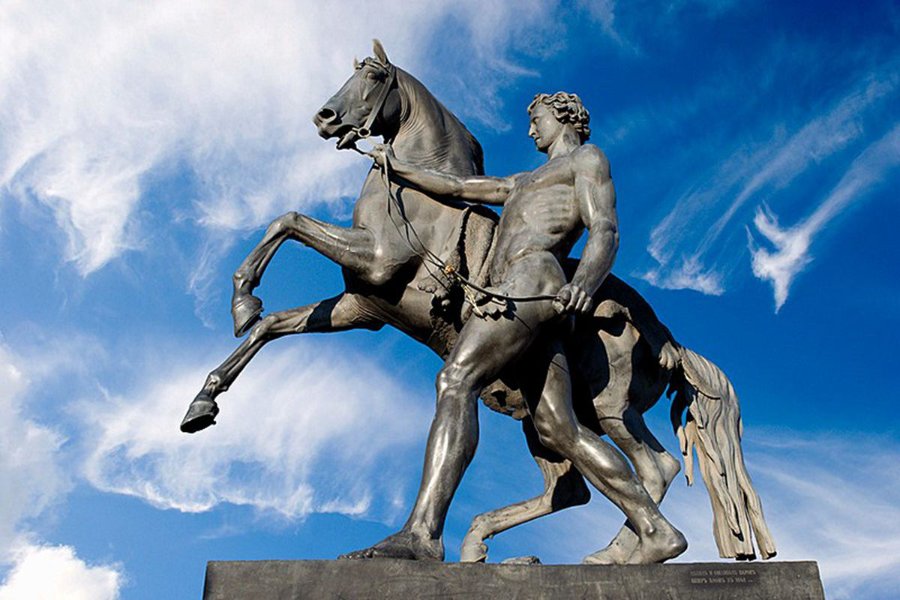A bronze Horse Tamers sculpture, set against a vibrant blue sky with scattered white clouds.