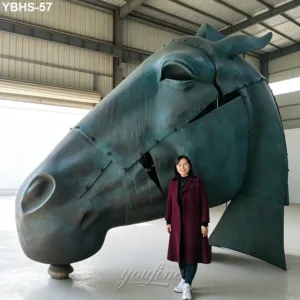 A monumental bronze horse head sculpture displayed indoors, accompanied by a woman standing beside it.