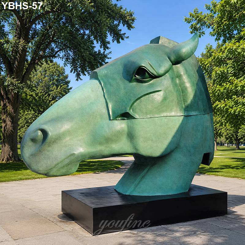 Large bronze horse head sculpture resting on a pedestal with trees and a sunny park background.