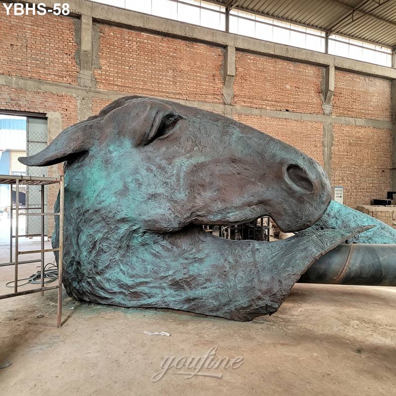 A large bronze horse head sculpture with a weathered green patina in a workshop.