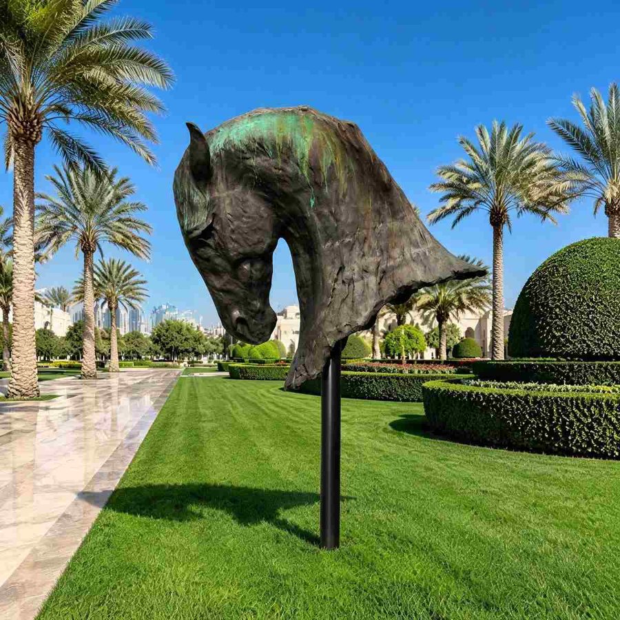 Bronze horse head statue on a pedestal in a manicured garden with palm trees, hedges, and a blue sky in the background.