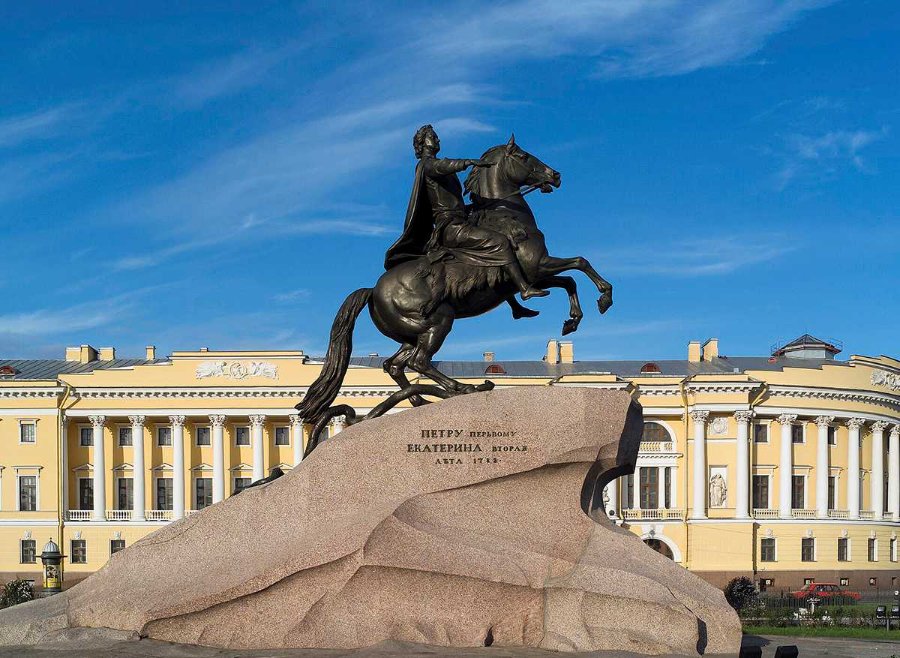 The Bronze Horseman equestrian statue of Peter the Great in Saint Petersburg, mounted on a granite pedestal with a yellow palace in the background.