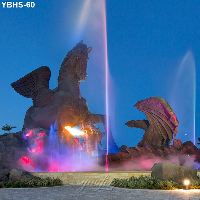 Bronze winged horse sculpture with a fire and water fountain, illuminated by colorful lights against a twilight sky.