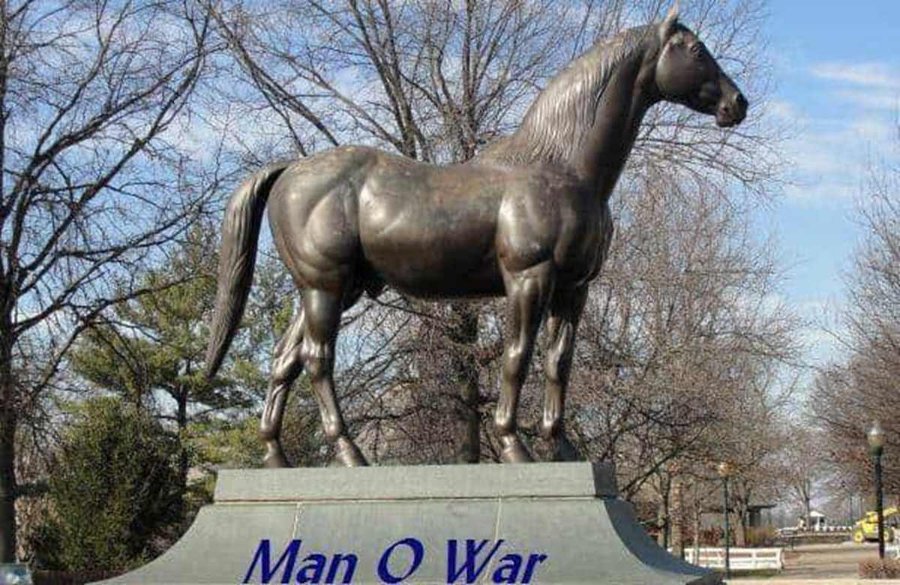 Bronze statue of the famous racehorse Man o' War, standing on a pedestal with its name inscribed, surrounded by trees and an open outdoor space.
