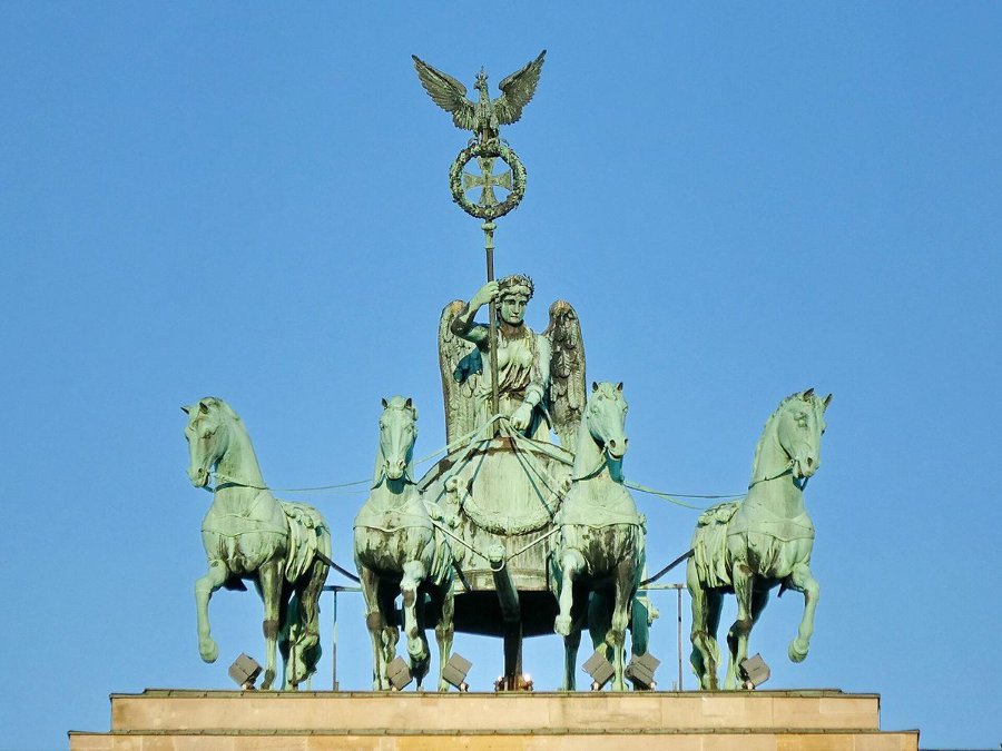 Quadriga sculpture featuring a chariot drawn by four horses, led by a winged figure holding a staff, atop the Brandenburg Gate in Berlin.