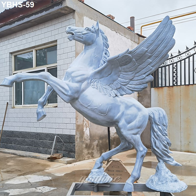 A white winged horse sculpture standing on two legs, captured in an outdoor setting near a tiled building and metal gate.