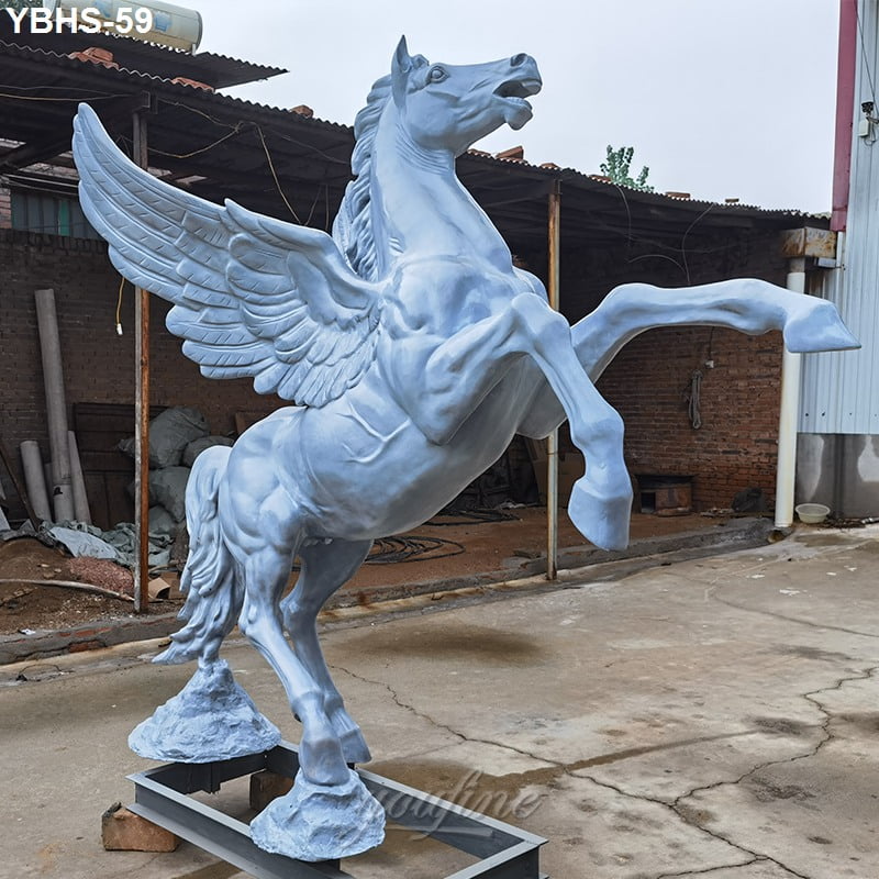 Large white Pegasus statue with detailed wings and raised front legs, crafted in a workshop setting with industrial surroundings.
