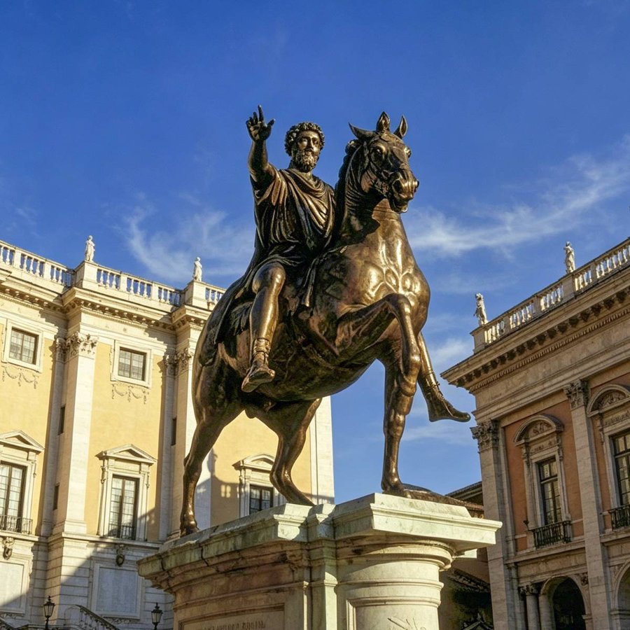 Bronze Marcus Aurelius equestrian statue of a historical figure on a horse, set against classical Roman-style architecture and a clear blue sky.