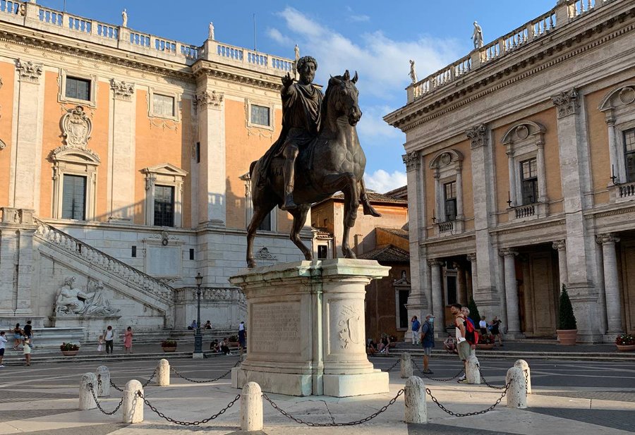 Bronze equestrian statue of Marcus Aurelius on a stone pedestal in the Piazza del Campidoglio, surrounded by historic buildings.